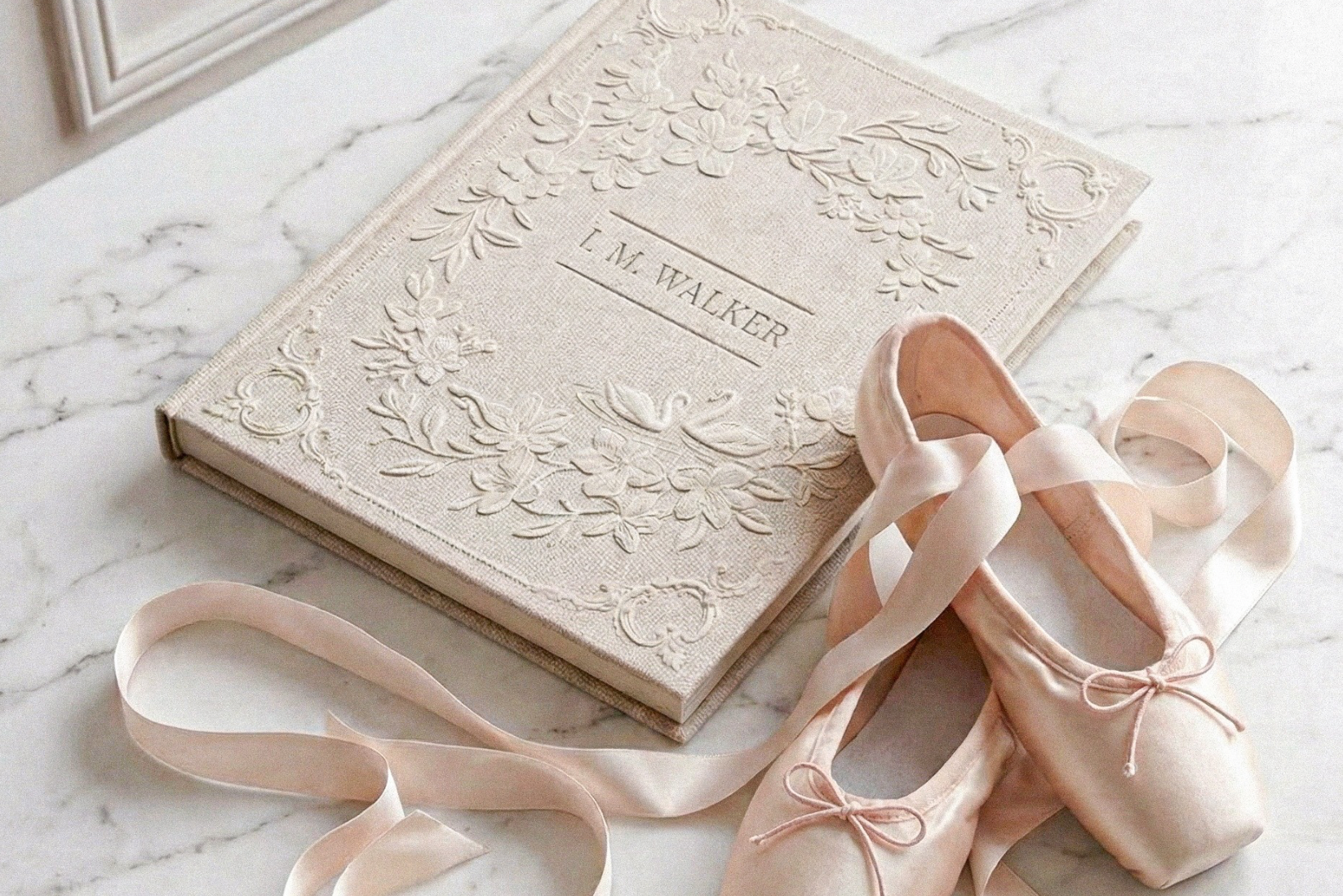 Ballet shoes with ribbons on a marble surface next to a book with the logo of fashion house I. M. WALKER.