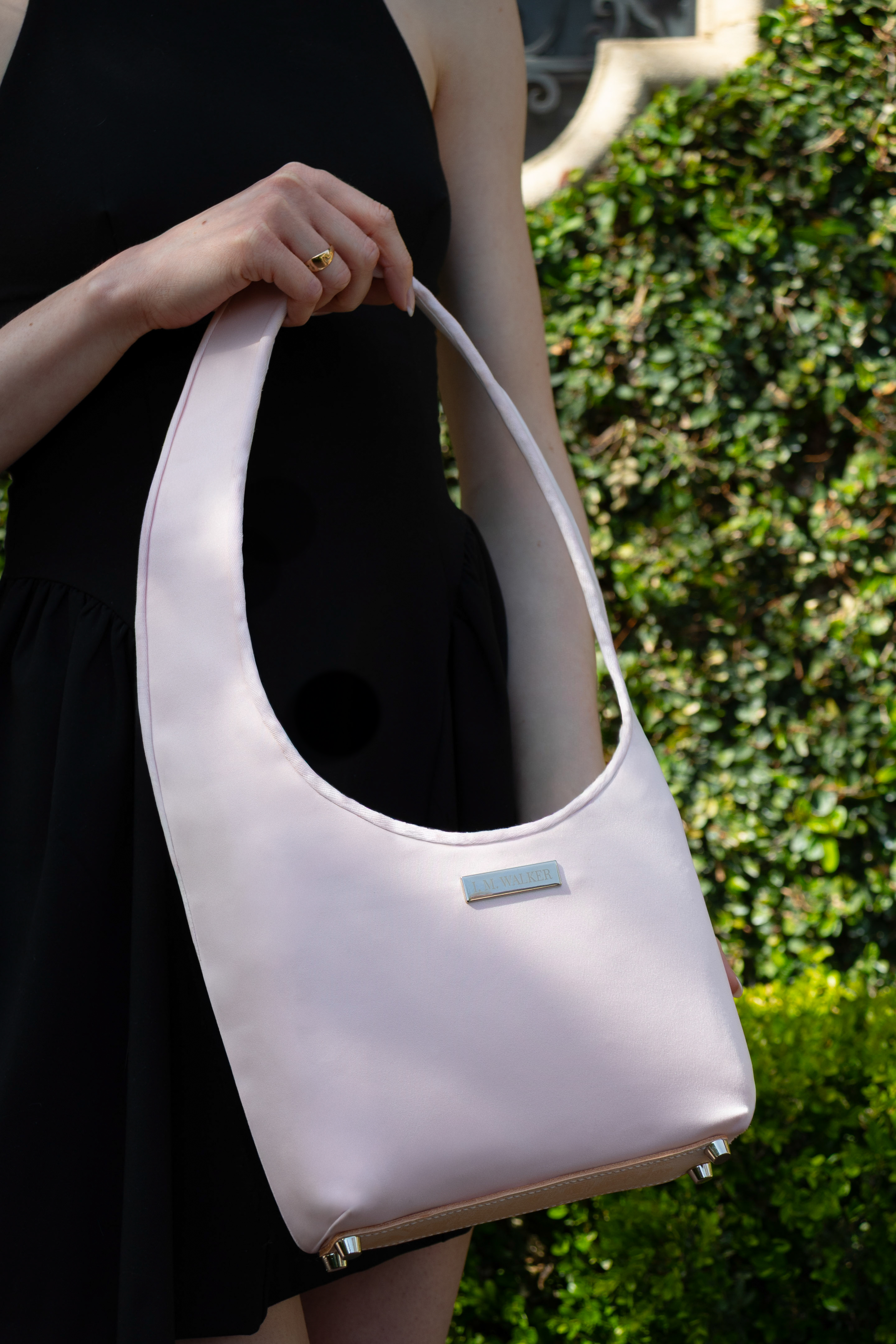 Woman holding an elegant pink satin handbag resembling a pointe shoe with a blurred green foliage background